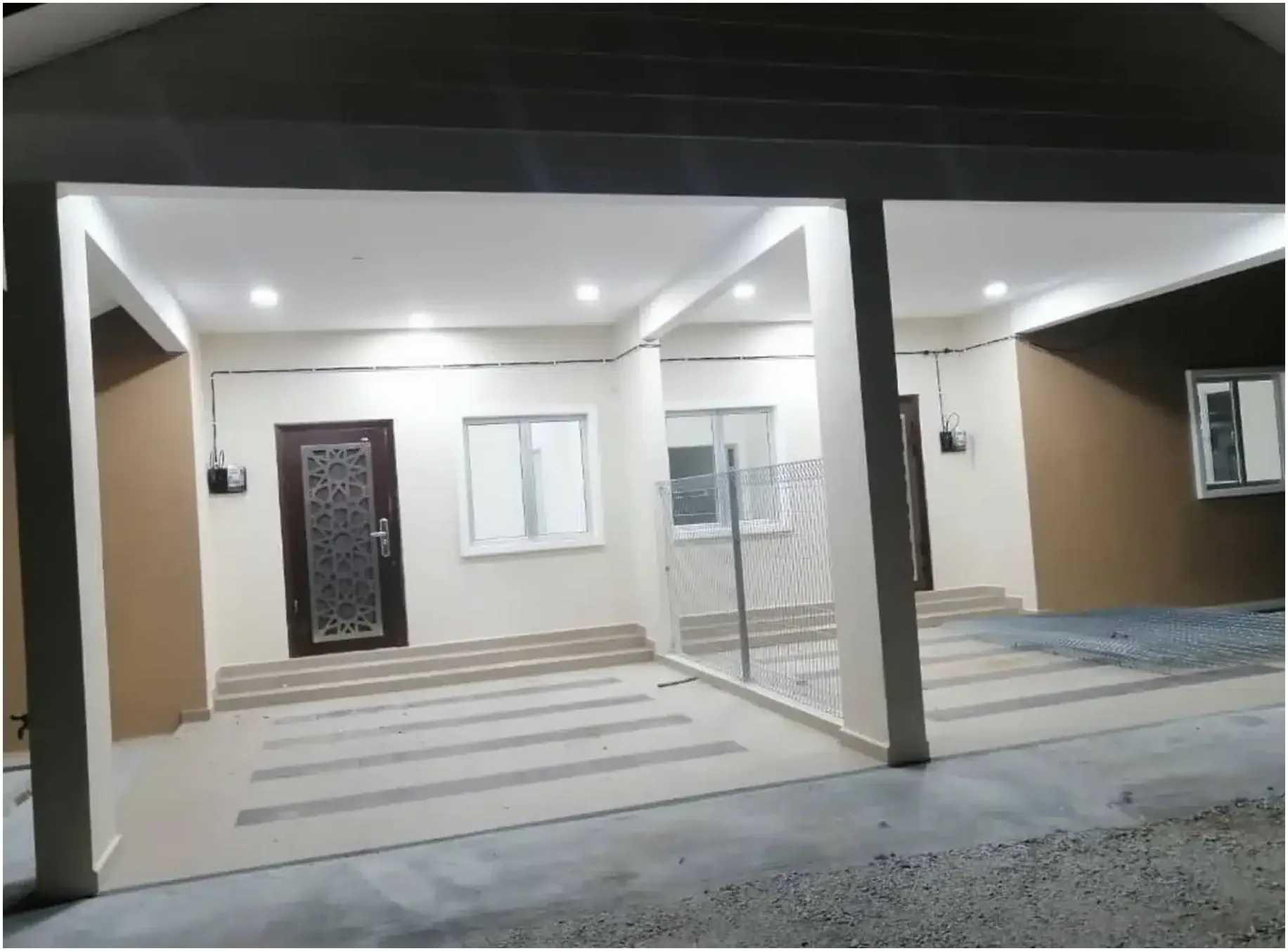 Porch rumah RumahHQ yang sudah siap pada waktu malam — dua kotak meter dipasang pada dinding dengan konduit permukaan, pintu grill besi dan lampu siling sudah menyala
